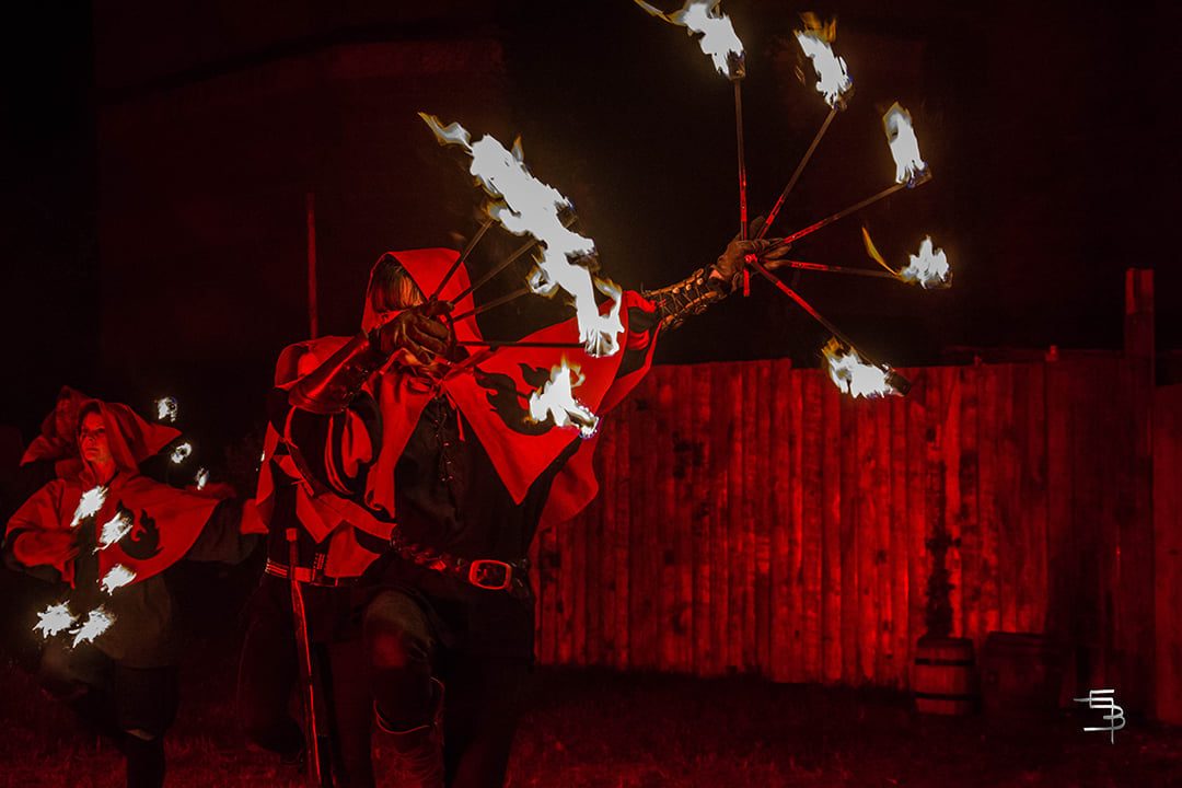 Comédien en cape rouge maniant des éventails de feu